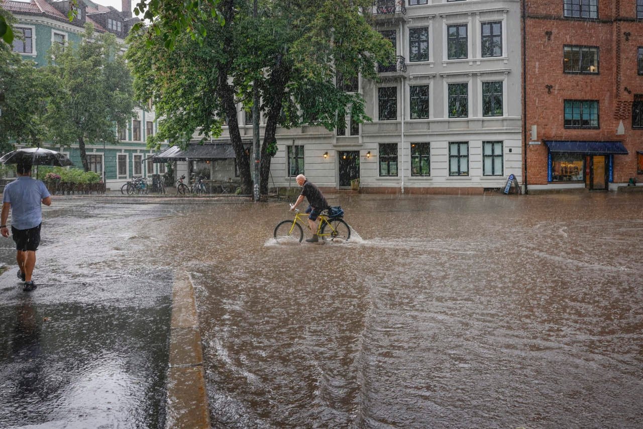 Finans Norges klimarapport 2025 viser en mann som går i oversvømte gater. Foto.