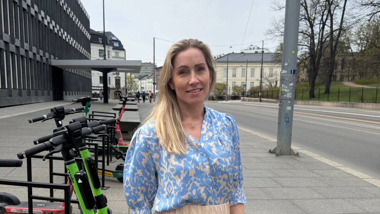 Line Hansen står på fortauet med elsparkesykler i bakgrunnen.