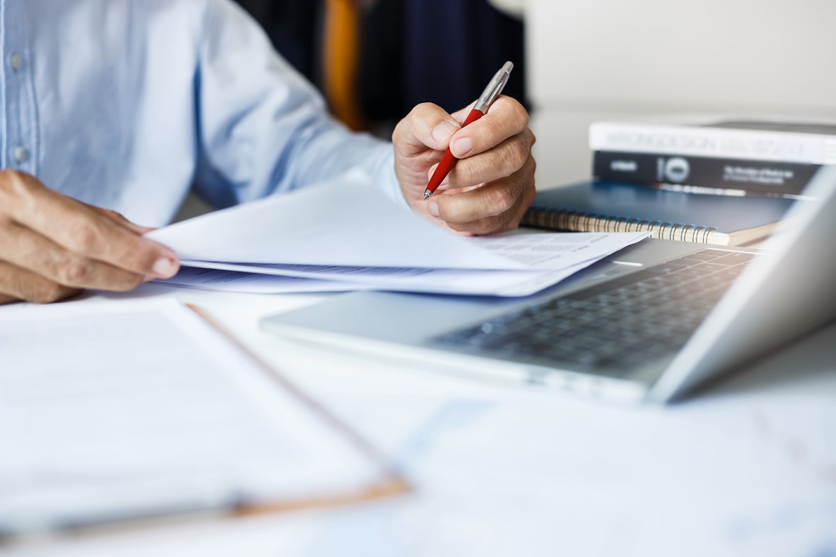 En person som holder en penn for å sjekke finansielle rapporter som ligger på pulten. Foto. 