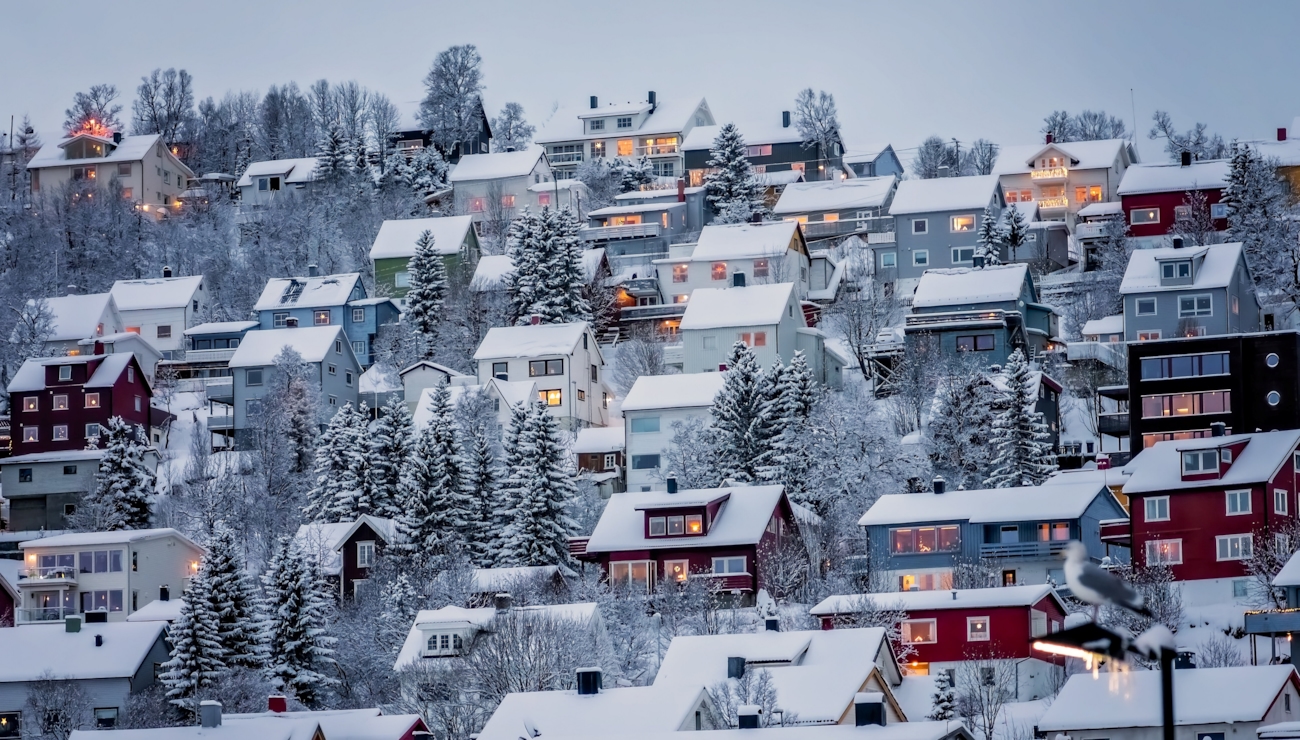 Mange hus på rekke og rad langs en fjellvegg i Tromsø. Husene er dekket av snø. Foto.