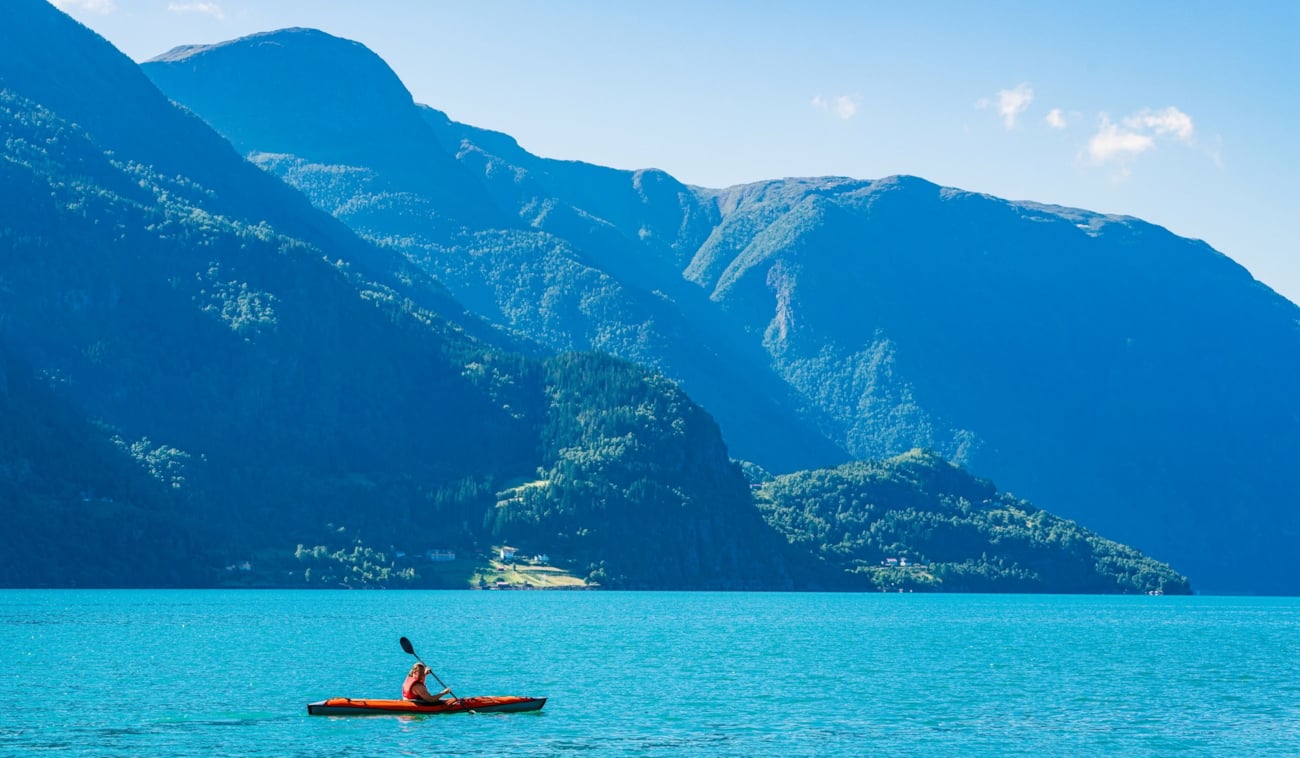 En person som padler i lyseblått brevann langs Norges fjord og fjell. Foto.