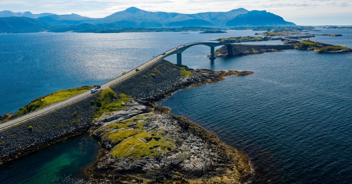Atlanterhavsvegen i Møre og Romsdal med utsikt over hav og fjell i solskinn. Foto.