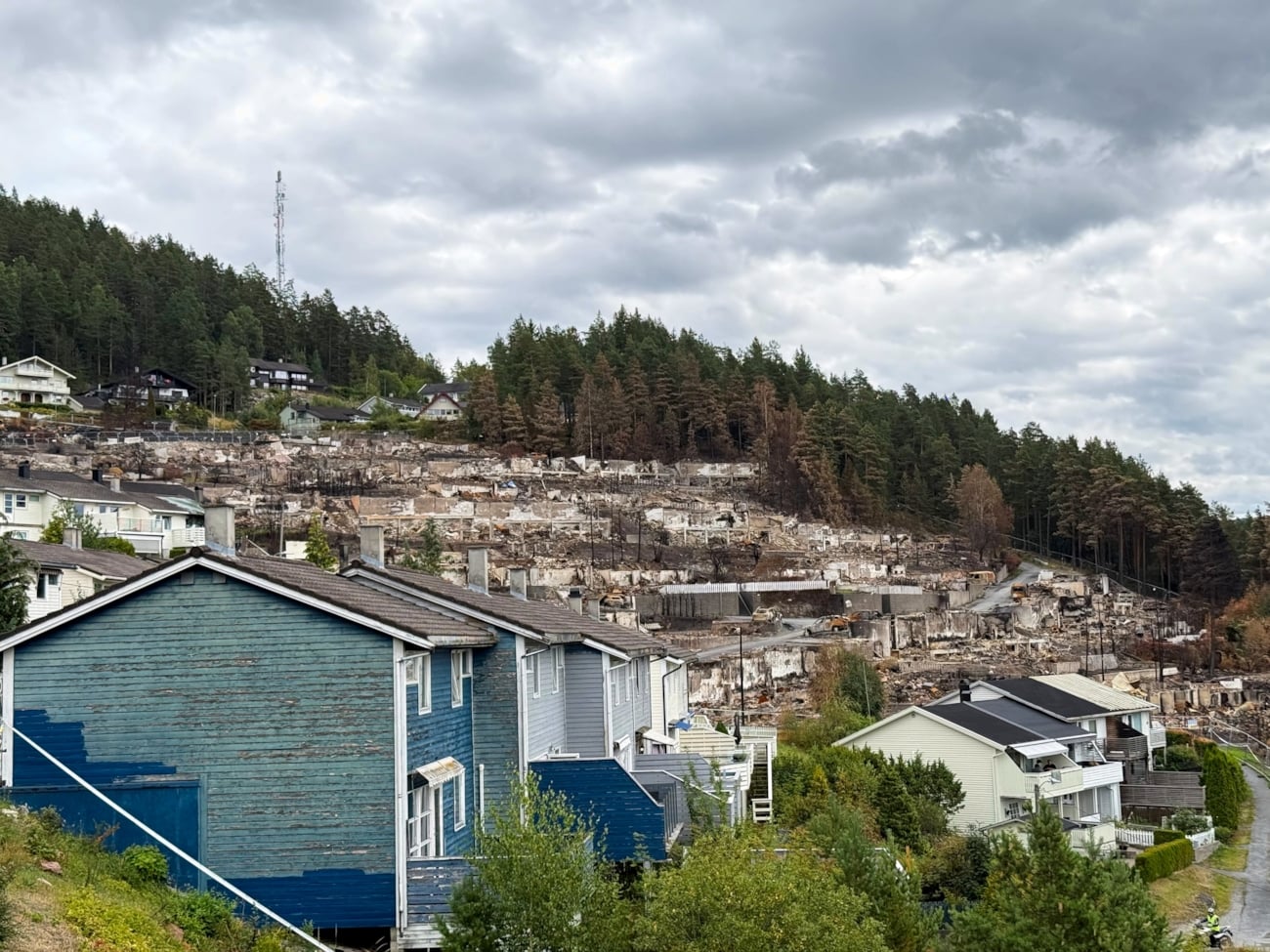 Boligområde i Krokstadelva etter brannen. Et blått hus står i forgrunnen, med det brannrammede området synlig i bakgrunnen.