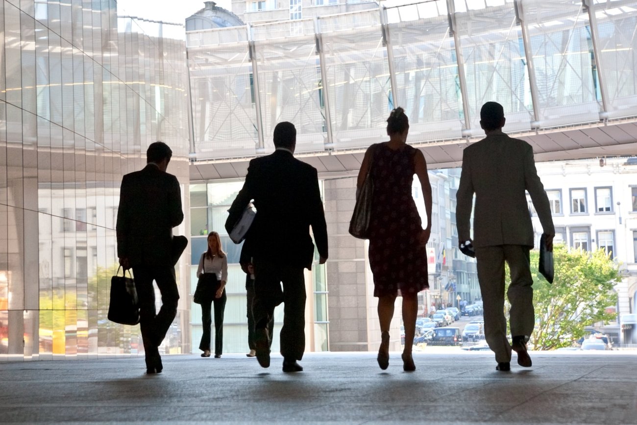 Silhuettene av fire forretningspersoner som går inne i en bygning med god belysning. Foto.