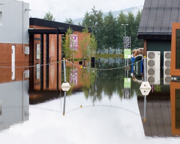 Parkeringsplass og bygninger som står i vann. Foto.