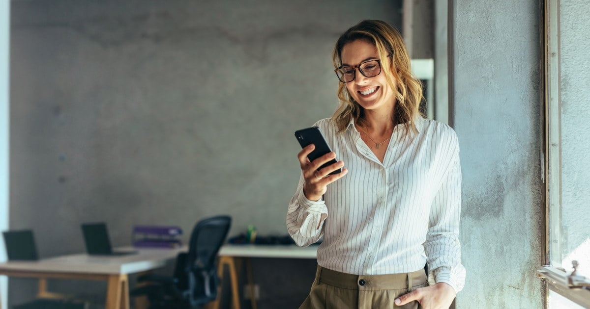 Kvinne i et kontorlandskap som ser på en mobil. Foto.