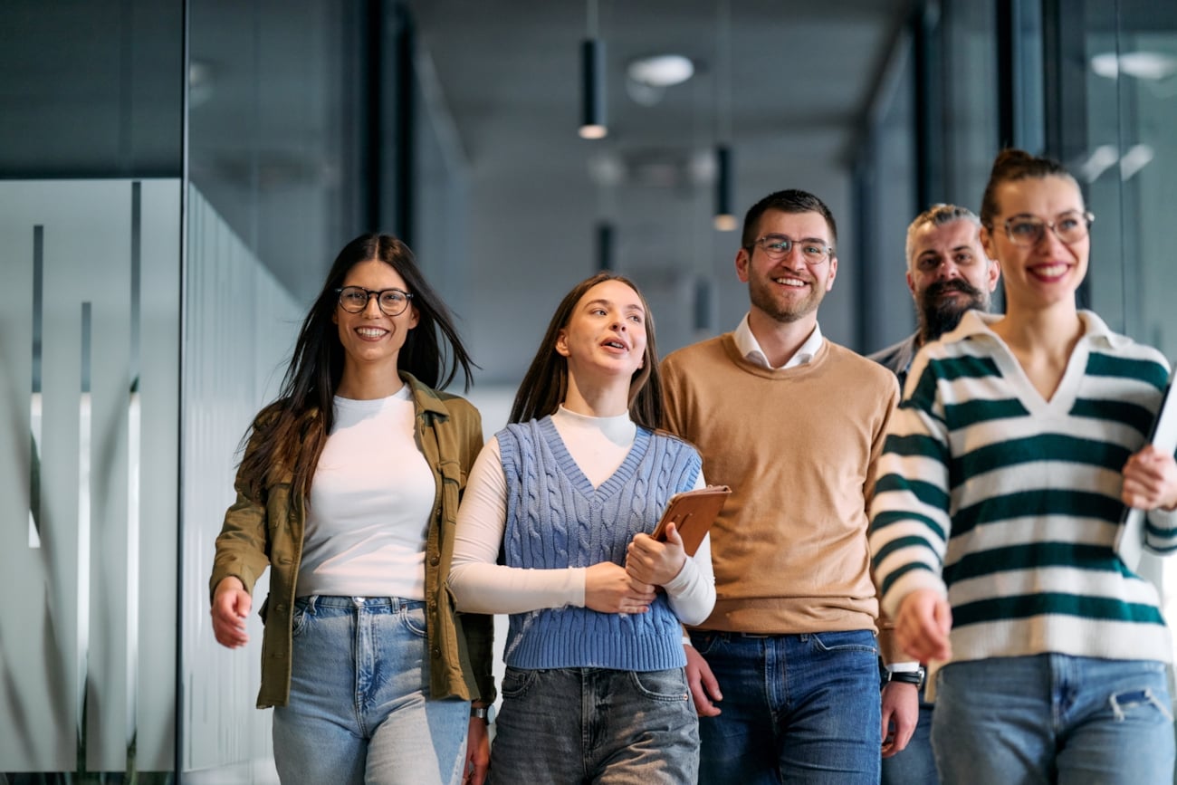 Fem personer på en arbeidsplass som kommer gående. Foto.