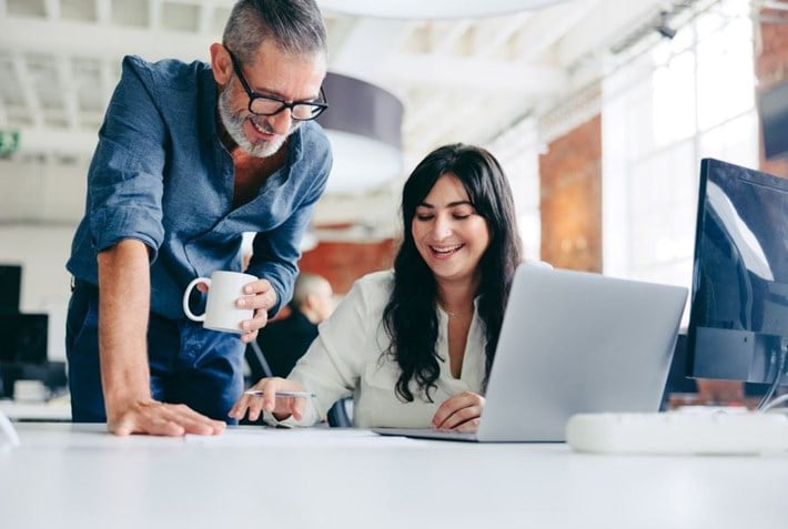 Bilde av en mann og en dame på et kontor, ser på papirer, holder en kaffe og smiler. 